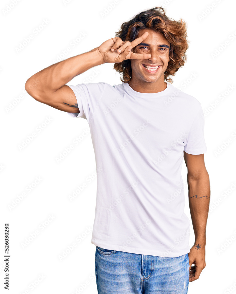 Young hispanic man wearing casual white tshirt doing peace symbol with fingers over face, smiling cheerful showing victory