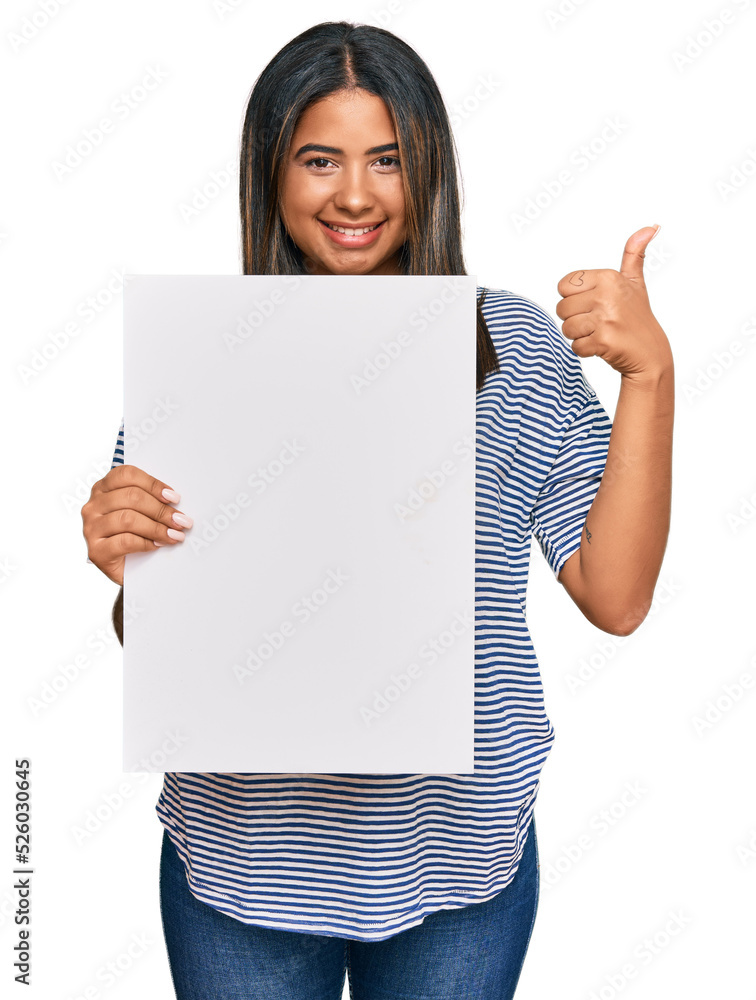 Young latin girl holding blank empty banner smiling happy and positive, thumb up doing excellent and approval sign Young latin girl holding blank empty banner smiling happy and positive, thumb up doing excellent and approval sign