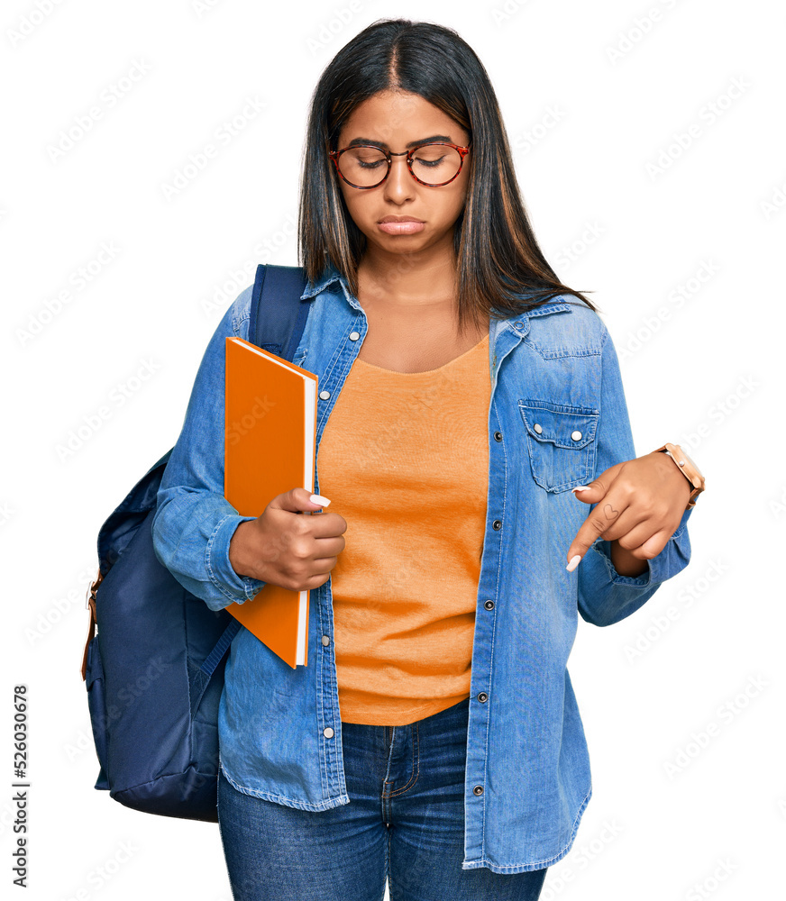 Young latin girl wearing student backpack and holding books pointing down looking sad and upset, indicating direction with fingers, unhappy and depressed. Young latin girl wearing student backpack and holding books pointing down looking sad and upset, indicating direction with fingers, unhappy and depressed.