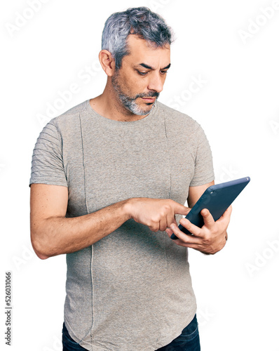 Middle age hispanic with grey hair using touchpad device relaxed with serious expression on face. simple and natural looking at the camera. photo