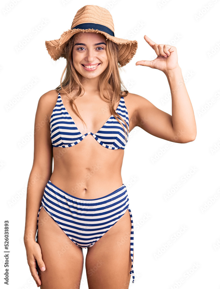 Young beautiful blonde woman wearing bikini and hat smiling and confident gesturing with hand doing small size sign with fingers looking and the camera. measure concept. Young beautiful blonde woman wearing bikini and hat smiling and confident gesturing with hand doing small size sign with fingers looking and the camera. measure concept.
