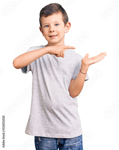 Cute blond kid wearing casual clothes amazed and smiling to the camera while presenting with hand and pointing with finger.