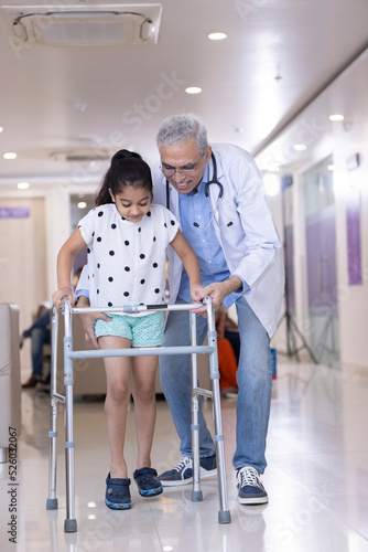 Male doctor teaching disabled girl to use walker at hospital 