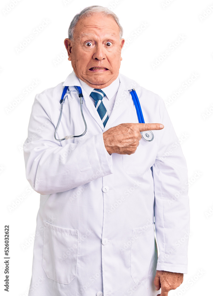 Senior handsome grey-haired man wearing doctor coat and stethoscope pointing aside worried and nervous with forefinger, concerned and surprised expression Senior handsome grey-haired man wearing doctor coat and stethoscope pointing aside worried and nervous with forefinger, concerned and surprised expression