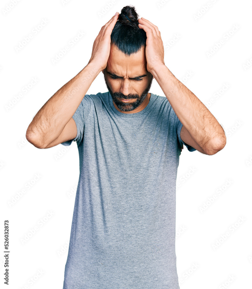 Hispanic man with ponytail wearing casual grey t shirt suffering from headache desperate and stressed because pain and migraine. hands on head. Hispanic man with ponytail wearing casual grey t shirt suffering from headache desperate and stressed because pain and migraine. hands on head.