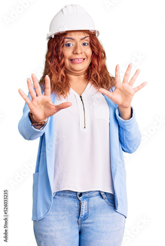 Young latin woman wearing architect hardhat afraid and terrified with fear expression stop gesture with hands, shouting in shock. panic concept.