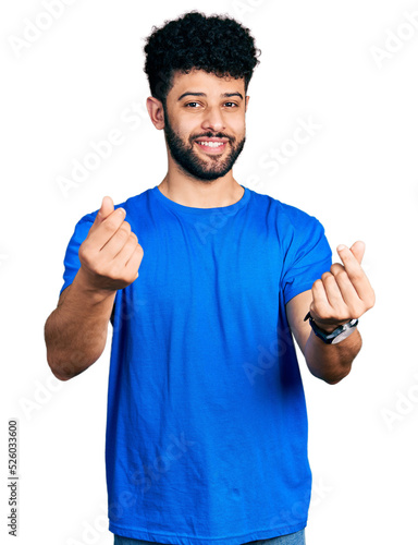 Young arab man with beard wearing casual blue t shirt doing money gesture with hands, asking for salary payment, millionaire business