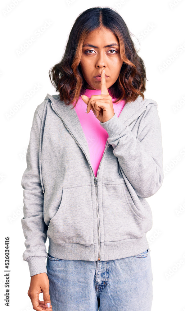 Young beautiful mixed race woman wearing casual sporty clothes asking to be quiet with finger on lips. silence and secret concept.