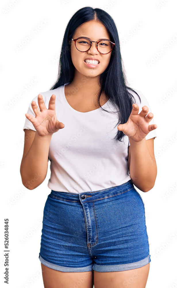 Young beautiful asian girl wearing casual clothes and glasses smiling funny doing claw gesture as cat, aggressive and sexy expression Young beautiful asian girl wearing casual clothes and glasses smiling funny doing claw gesture as cat, aggressive and sexy expression