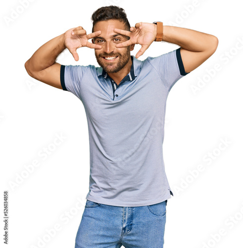 Handsome man with beard wearing casual clothes doing peace symbol with fingers over face, smiling cheerful showing victory