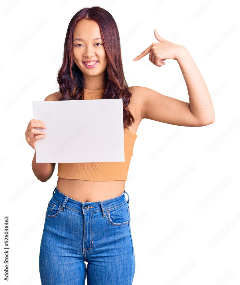 Young beautiful chinese girl holding paper banner with blank space pointing finger to one self smiling happy and proud Young beautiful chinese girl holding paper banner with blank space pointing finger to one self smiling happy and proud