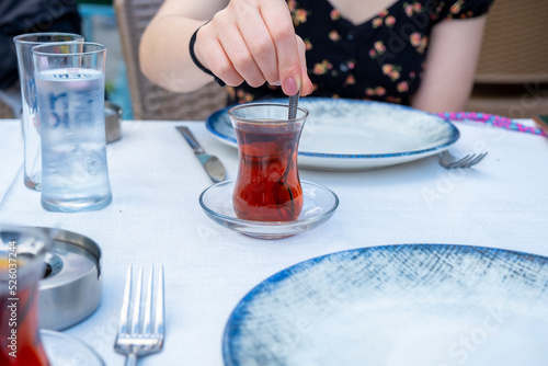 Woman hand stirring traditional Turkish tea, Turkish raki on the background, Turkey pub and raki drink concept, sitting view, Turkish drink idea, mixing tea photo