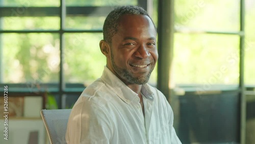 Portrait of a happy african american man turns his head to look at the camera smiling. Sitting in office. Businessman, entrepreneur, CEO. Corporate business. Slow motion