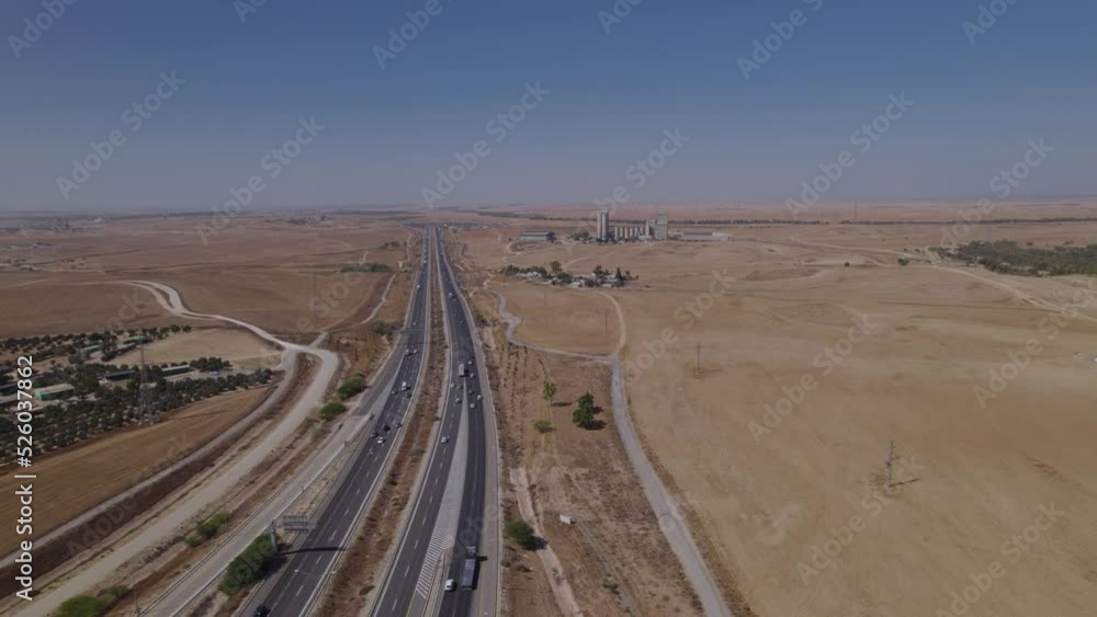 Aerial shot near a highway in a dry and desert area, a non-urban area, the suburbs of the city, some buildings of the landowners and an old factory in the distance Aerial shot near a highway in a dry and desert area, a non-urban area, the suburbs of the city, some buildings of the landowners and an old factory in the distance
