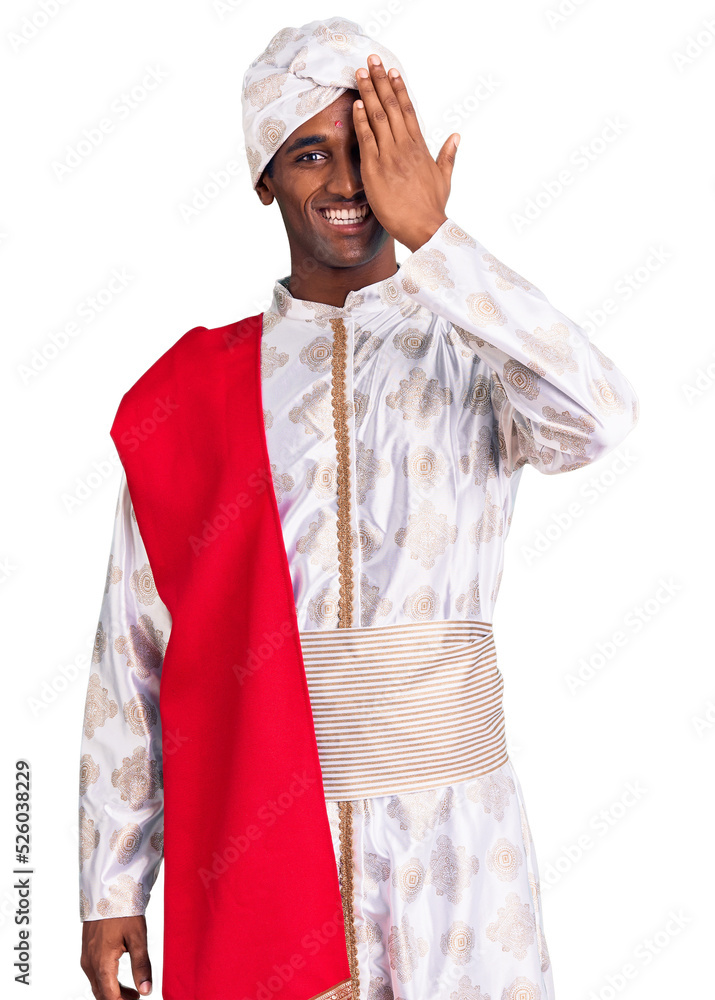 African handsome man wearing tradition sherwani saree clothes covering one eye with hand, confident smile on face and surprise emotion. African handsome man wearing tradition sherwani saree clothes covering one eye with hand, confident smile on face and surprise emotion.