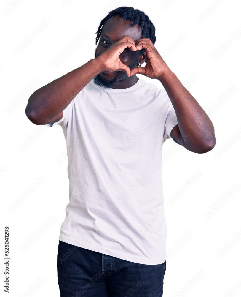 Young african american man with braids wearing casual white tshirt doing heart shape with hand and fingers smiling looking through sign Young african american man with braids wearing casual white tshirt doing heart shape with hand and fingers smiling looking through sign