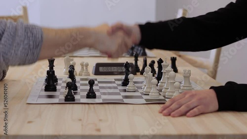 The player understands that he has lost and gives up, stops the timer, the players shake hands. Two men plays in rapid chess on wooden table close up photo