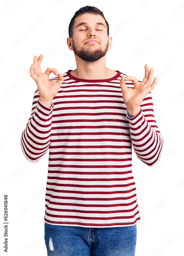 Young handsome man wearing striped sweater relaxed and smiling with eyes closed doing meditation gesture with fingers. yoga concept. Young handsome man wearing striped sweater relaxed and smiling with eyes closed doing meditation gesture with fingers. yoga concept.