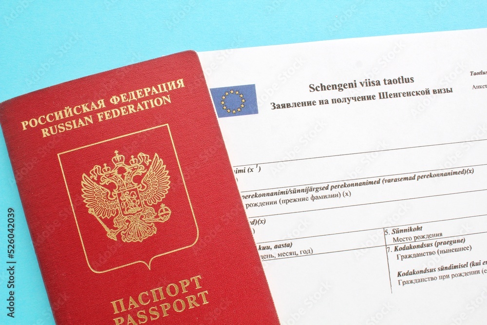 Schengen visa application form in Russian and Estonian language and passport on blue background. Prohibition and suspension of visas for Russian tourists to travel to Europe Union and Baltic States Schengen visa application form in Russian and Estonian language and passport on blue background. Prohibition and suspension of visas for Russian tourists to travel to Europe Union and Baltic States