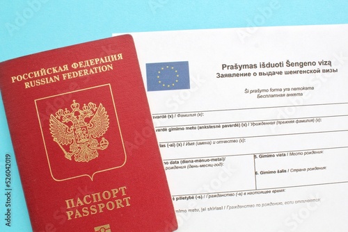 Schengen visa application form in Russian and Lithuanian language and passport on blue background. Prohibition and suspension of visas for tourists travel to Europe Union and Baltic States concept