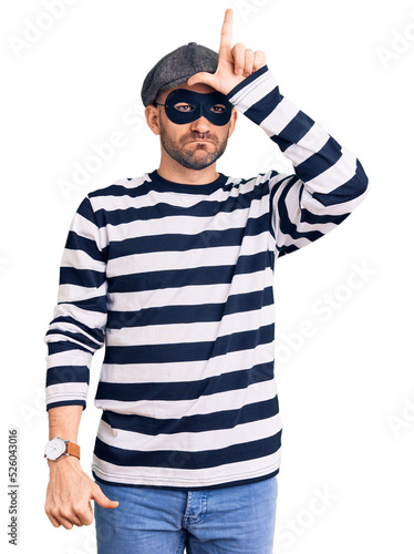 Young handsome man wearing burglar mask making fun of people with fingers on forehead doing loser gesture mocking and insulting. © Krakenimages.com