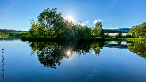 Beautiful early summer landscape with green grass, blue sky and amazing reflection in river © smaliariryna