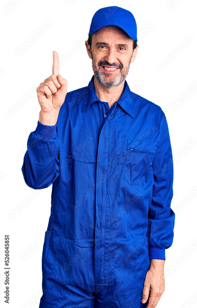 Middle age handsome man wearing mechanic uniform showing and pointing up with finger number one while smiling confident and happy.