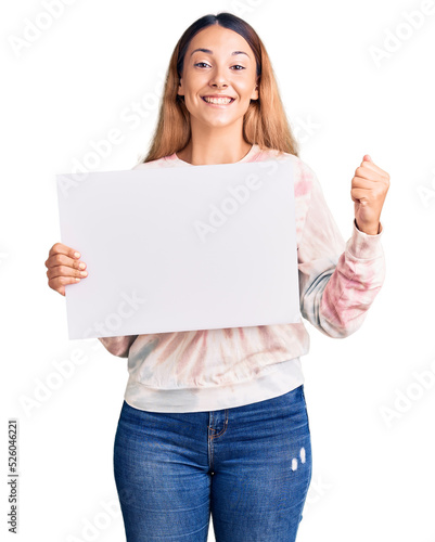 Beautiful young woman holding blank empty banner screaming proud, celebrating victory and success very excited with raised arms