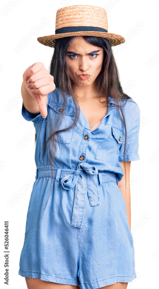 Brunette teenager girl wearing summer hat looking unhappy and angry showing rejection and negative with thumbs down gesture. bad expression. Brunette teenager girl wearing summer hat looking unhappy and angry showing rejection and negative with thumbs down gesture. bad expression.