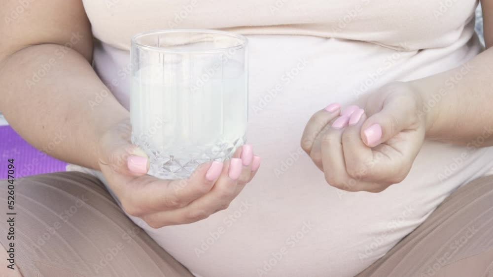 pregnant woman hold one glass with water and 2 round pills tablets