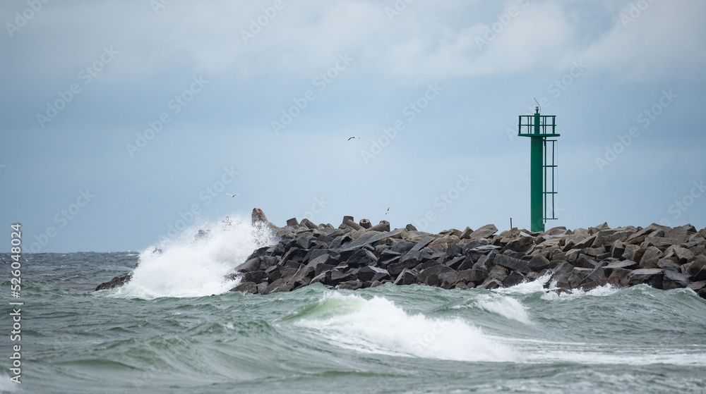A storm in the Baltic Sea. Rough sea in the background a concrete breakwater with a lighthouse. Waves in the Baltic Sea, foamy water.