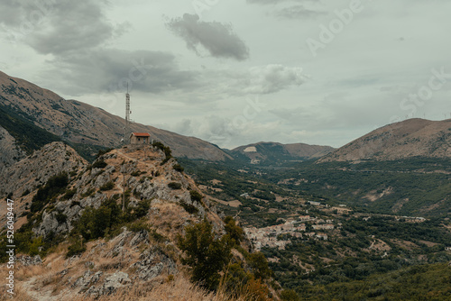 mountain landscape with rock and overcast sky during a summer hike. On the edge of the mountain we see a lonely house