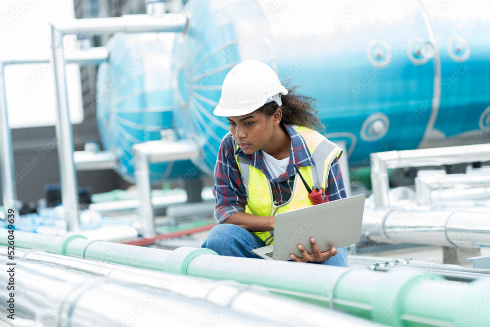 © amorn - Female engineer work using laptop computer for checks or maintenance in sewer pipes area at construction site. African American woman engineer working in sewer pipes area at rooftop of building © amorn - Female engineer work using laptop computer for checks or maintenance in sewer pipes area at construction site. African American woman engineer working in sewer pipes area at rooftop of building
