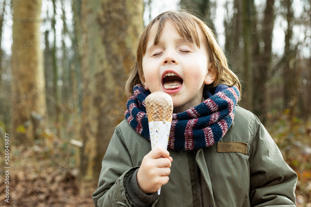 Toddler boy wearing warm jacket and scarf eating chocolate ice cream in waffle cone with pleasue, outdoor in cold weather. Toddler boy wearing warm jacket and scarf eating chocolate ice cream in waffle cone with pleasue, outdoor in cold weather.
