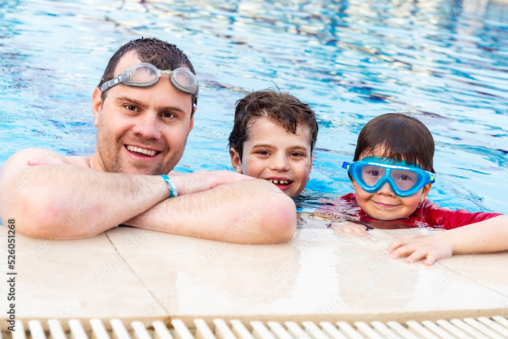 Obraz na plátně Father with two sons spending time in a swimming pool in a hotel in summer