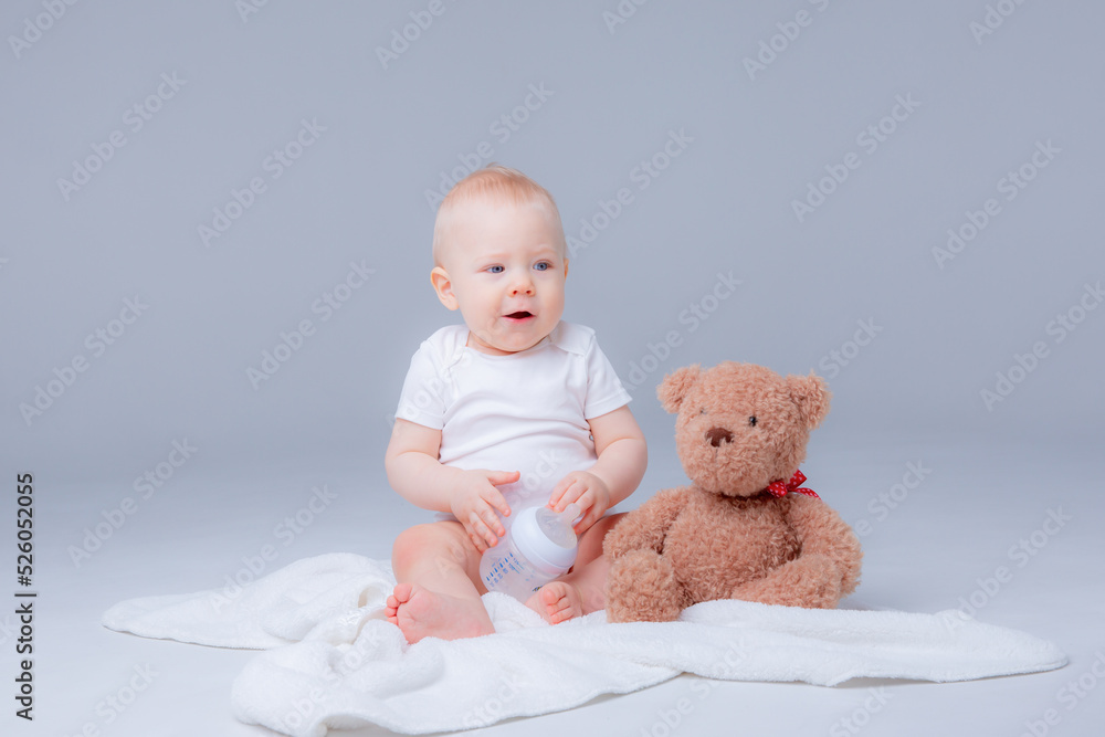 a baby boy in a white bodysuit sits with a teddy bear on a white background, holding a bottle of water , drinking water a baby boy in a white bodysuit sits with a teddy bear on a white background, holding a bottle of water , drinking water