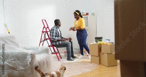 African american couple planning renovation on new home. Portrait of wife and husband sitting on ladder discuss new design living room. photo