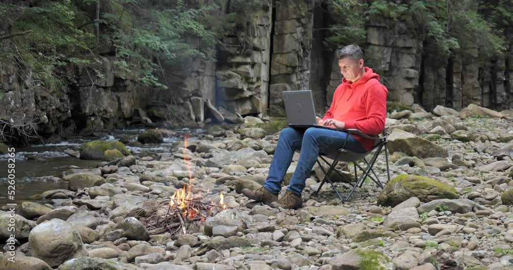 A man works on a laptop near a stream in nature A man works on a laptop near a stream in nature