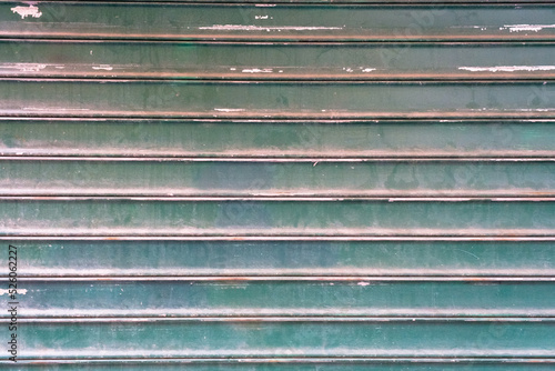 Dirty textured steel garage door painted in green, background, striped metal colored shutter wall, abstract horizontal lines, grunge texture and pattern.