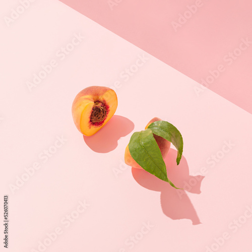 Trendy fresh fruit composition made of cut peach slices with pit and leaves and sunshine shadows. Minimal pastel peach pink background. Creative healthy food concept. Romantic summer party aesthetic.