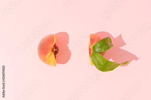 Fresh juicy peach with pit and leaves cut in half on pastel pink background. Minimal fruit concept. Healthy raw food trendy composition. Summer party aesthetic. Flat lay.