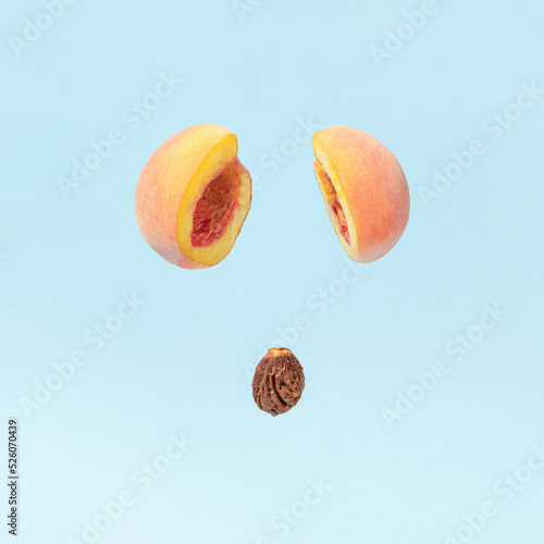 Peach pit dropping from two cut halves of fresh peach against pastel blue background. Creative fruit concept. Minimal healthy food composition.