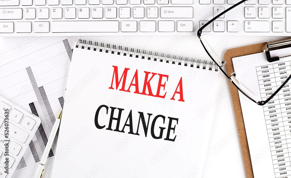 Text MAKE A CHANGE on Office desk table with keyboard, notepad and analysis chart on white background.