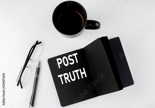 POST TRUTH written text in small black notebook with coffee , pen and glasess on a white background. Black-white style
