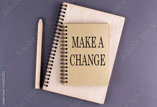 Word MAKE A CHANGE a notebook with pencil on the grey background