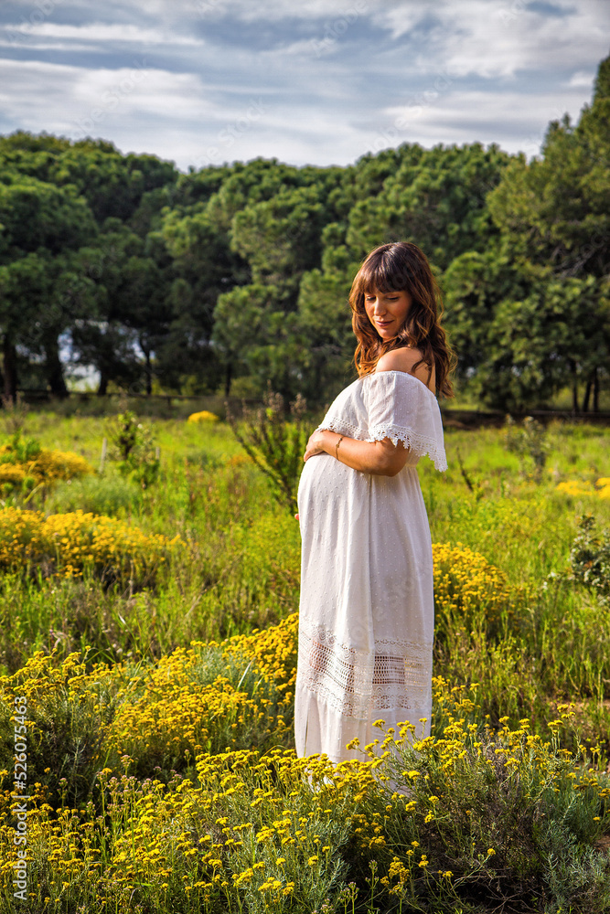 A young pregnant woman in a field touching her pregnancy belly A young pregnant woman in a field touching her pregnancy belly