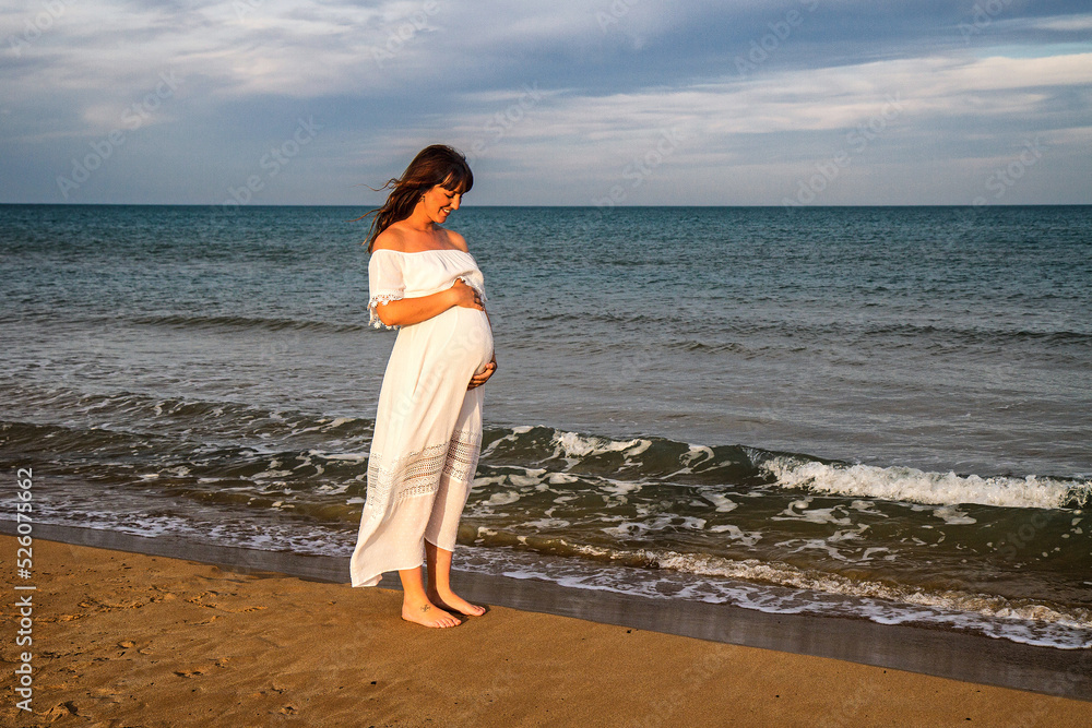 A young pregnant woman on a beach touching her pregnancy belly