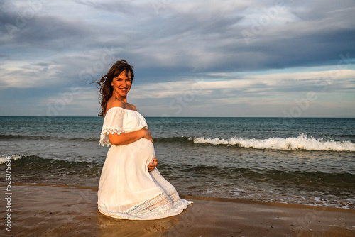 A young pregnant woman on a beach touching her pregnancy belly