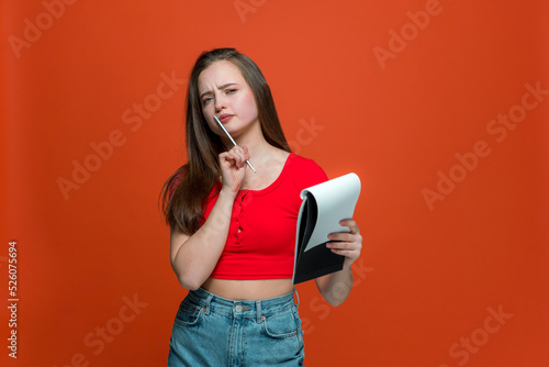 Creative young modern girl with notepad and pencil think out ideas for project, make to do list on orange background