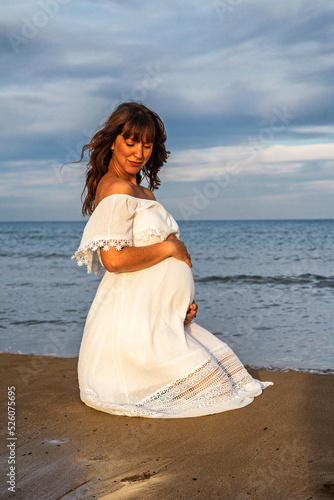 A young pregnant woman on a beach touching her pregnancy belly